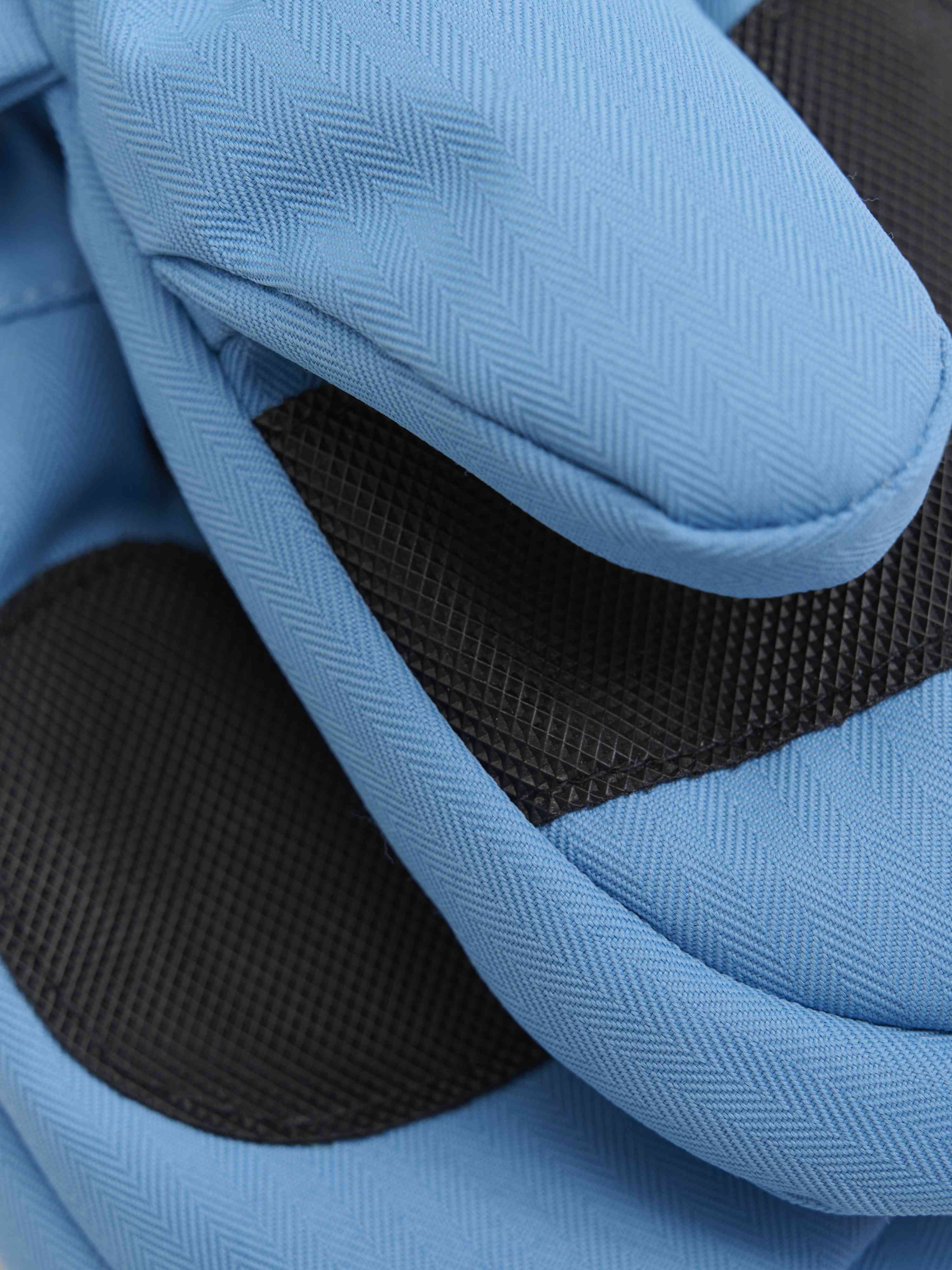Nahaufnahme der Color Kids - Handschuhe W. Zipper, aus einem blau strukturierten Stoff mit schwarzen Mesh-Akzenten. Dieser Schutzhandschuh von Color Kids besteht aus recyceltem Material und weist ein Fischgrätenmuster mit Nähten auf, die eine Polsterung oder Verstärkung suggerieren.