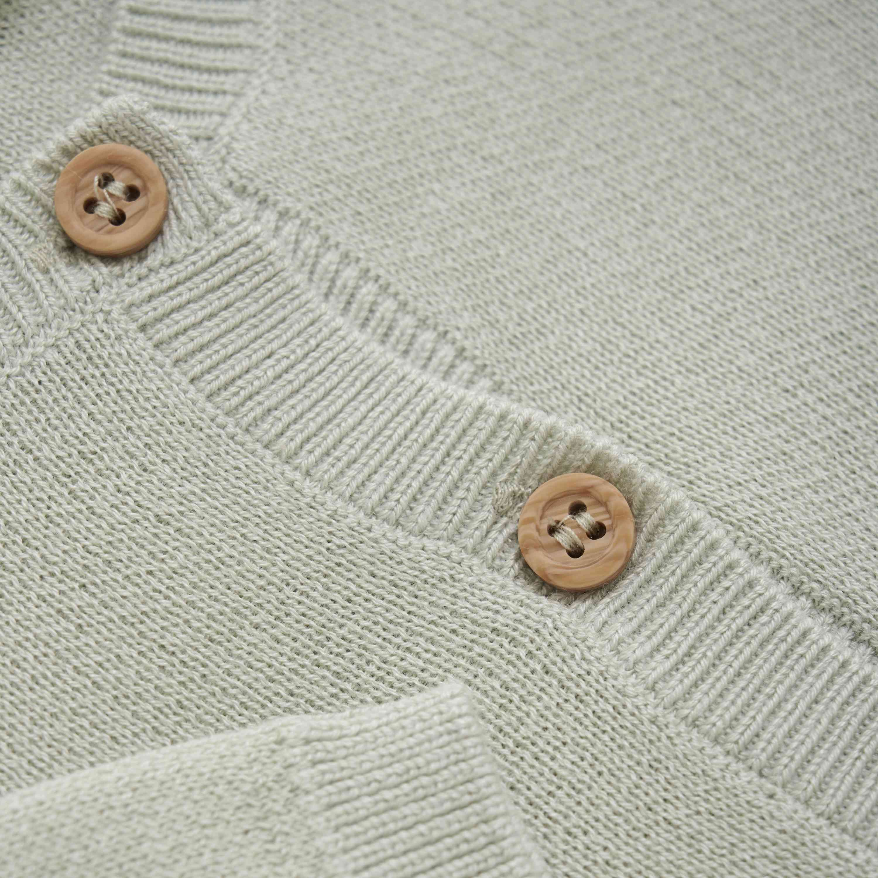 Nahaufnahme eines hellgrünen Fixoni - Cardigan Knit mit zwei Holzknöpfen. Die Textur des Strickgewebes aus weichem Bambusstoff und die Details der gerippten Kanten um den Knopfbereich sind sichtbar und betonen die Qualität und Handwerkskunst des Kleidungsstücks von Fixoni.